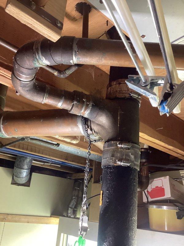 # Plumbing Leak Inspection and Assessment

Responded to reported leak in cast iron and copper piping system located in basement of 1960s-era residential property. Conducted thorough visual inspection of exposed plumbing infrastructure in basement ceiling area, including cast iron drain lines and copper water supply lines. 

Inspection revealed aging plumbing system with multiple pipe materials typical of 1960s construction standards. Examined cast iron waste lines for signs of corrosion, deterioration, and active leaking. Assessed copper supply piping for pinhole leaks, corrosion, and joint integrity. Photographed affected areas showing overhead plumbing configuration, including PVC drainage lines, insulated pipe sections, and mechanical components suspended from floor joists.

Documentation captured exposed wooden joist structure with various plumbing materials secured by metal hangers and straps. Noted presence of moisture or condensation on mechanical equipment, which required furth