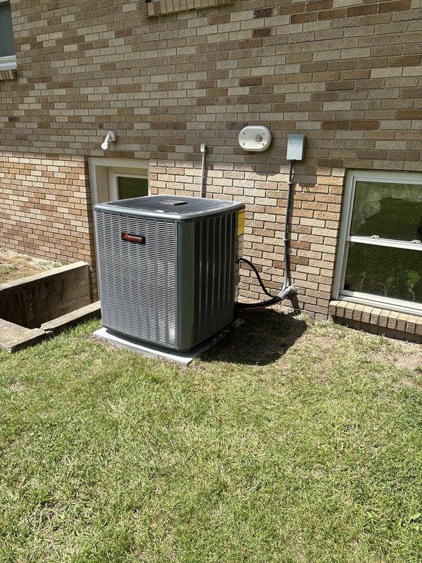 Completed full HVAC system installation including new furnace and air conditioning unit. Indoor furnace unit installed in basement/utility room with proper PVC intake and exhaust venting, mounted on drip pan with auxiliary condensate management system and connected ductwork. Outdoor condenser unit positioned on pad against exterior wall with electrical conduit and refrigerant lines properly routed through brick facade. All components tested and operational upon completion.