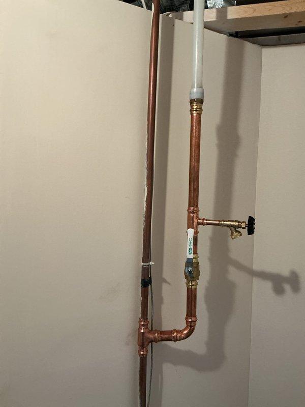 Installed new irrigation line with copper piping and PVC connections, running from interior plumbing through exterior wall with proper brass fittings, valves, and shut-off controls. Work included vertical and horizontal pipe runs with T-junction installation and pressure regulation components to support new irrigation system functionality.