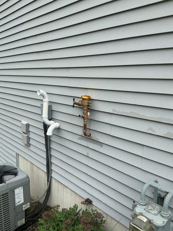Installed new irrigation line with copper piping and PVC connections, running from interior plumbing through exterior wall with proper brass fittings, valves, and shut-off controls. Work included vertical and horizontal pipe runs with T-junction installation and pressure regulation components to support new irrigation system functionality.