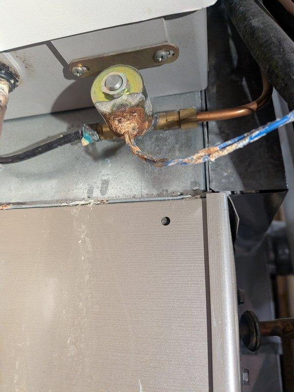 Responded to service call for air conditioning unit experiencing water leakage onto floor. Upon inspection, discovered condensate drain line obstruction and significant corrosion on humidifier solenoid valve assembly. Cleared clogged PVC condensate drain line to restore proper drainage from evaporator coil. Assessed heavily corroded humidifier valve and connecting components, which customer had previously shut off due to deterioration. Documented existing corrosion damage on valve body and mounting hardware for customer records. Verified condensate system now draining properly and provided recommendations for humidifier valve replacement to prevent future water leak issues.