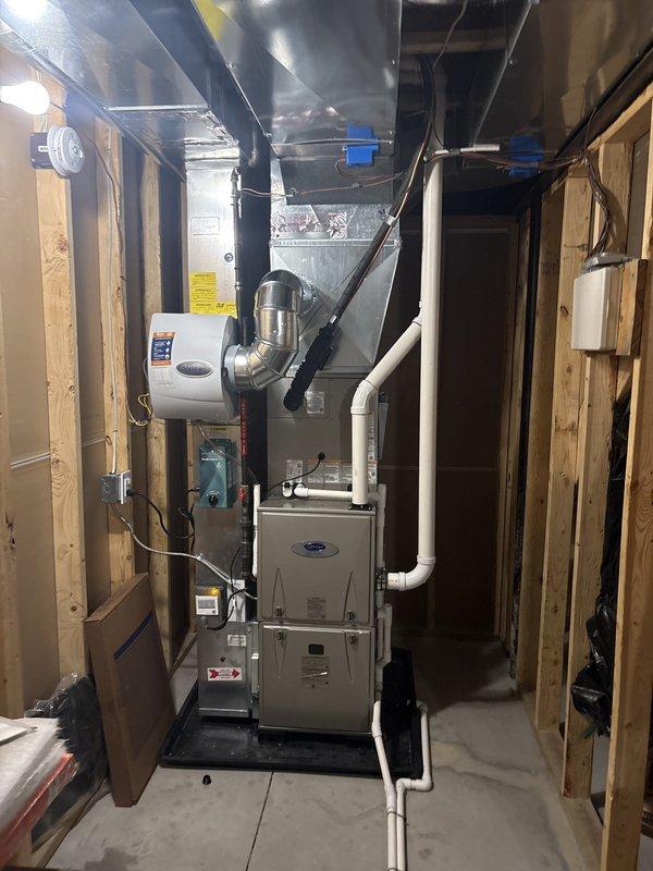 Completed full air conditioning system replacement in residential basement mechanical room. Installed new Carrier furnace unit with integrated cooling coil, connected to existing ductwork infrastructure including metal plenums and rectangular trunk lines. Established proper condensate drainage using white PVC piping, integrated wall-mounted humidifier unit with metallic flex duct connections, and verified all electrical connections and control wiring. System tested and confirmed operational with proper airflow distribution through existing duct network.