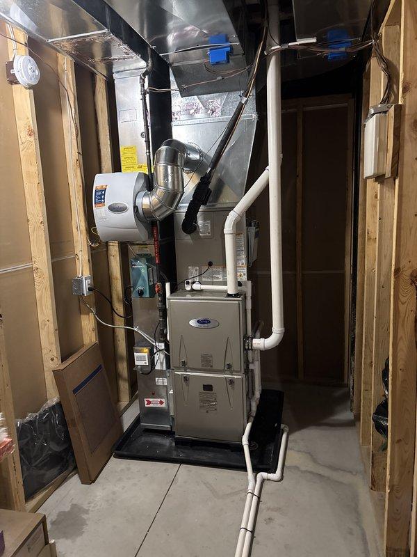 Completed full air conditioning system replacement in residential basement mechanical room. Installed new Carrier furnace unit with integrated cooling coil, connected to existing ductwork infrastructure including metal plenums and rectangular trunk lines. Established proper condensate drainage using white PVC piping, integrated wall-mounted humidifier unit with metallic flex duct connections, and verified all electrical connections and control wiring. System tested and confirmed operational with proper airflow distribution through existing duct network.