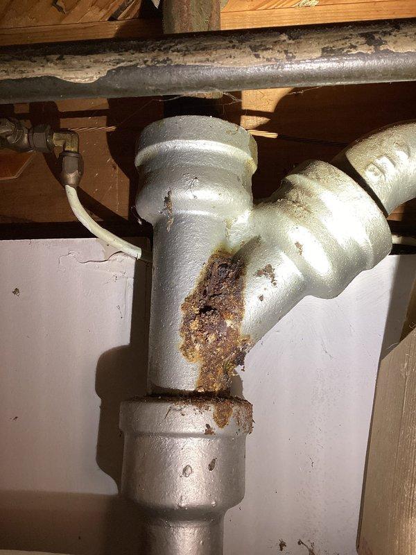 Responded to laundry room washer drain overflow that had been occurring for several weeks. Upon arrival, inspected the drainage system and plumbing infrastructure. Observed aged galvanized piping with significant corrosion, oxidation, and rust-colored mineral deposits on vertical drain lines. Snaked the washer drain line to clear the blockage causing the overflow condition. Verified proper drainage flow after clearing obstruction. Documented existing plumbing conditions showing deteriorated galvanized pipes with visible patina and corrosion throughout the drainage assembly. Issue resolved with drain now flowing freely without backup into laundry room.