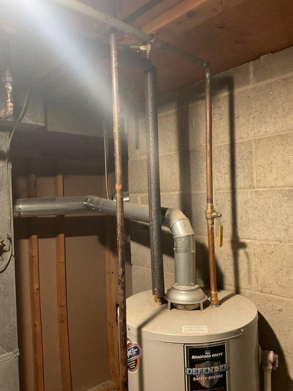 Responded to service call for 15-year-old Bradford White Defender water heater with non-functioning thermometer preventing proper heating and hot water recognition. Addressed slow leak originating from gasket area. Upon inspection, documented existing water damage evidenced by yellow staining on overhead plywood sheathing, indicating previous or ongoing moisture intrusion from the leaking gasket. Assessed condition of water heater connections, copper supply lines, and associated plumbing components in basement mechanical room.