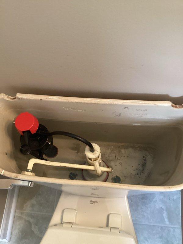 Responded to plumbing leak complaint regarding toilet supply line. Upon arrival, inspected toilet tank interior and identified aging fill valve assembly with red plastic cap component and associated black plastic fittings showing signs of wear and mineral buildup. Examined chrome angle stop valve and braided stainless steel supply line connection at wall. Verified shut-off valve operation and confirmed proper function of water supply control. Documented existing conditions including significant mineral deposits and water staining throughout tank interior, indicating prolonged exposure and age of fixture components. Assessed float mechanism and linkage assembly for proper operation. Leak source identified and addressed to restore proper function of toilet supply system.