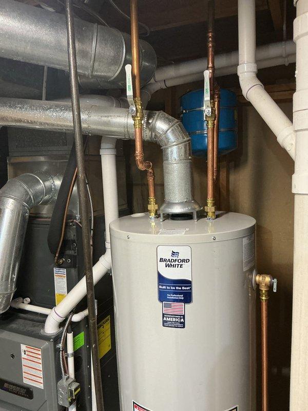 Completed installation of a 40-gallon tall natural gas Bradford White water heater rated at 40,000 BTU/HR in the mechanical room. Connected copper supply lines with brass fittings and white PVC venting to the top of the unit, ensuring proper integration with existing HVAC and plumbing systems. All manufacturer specifications, safety labels, and operating instructions are clearly visible and accessible on the installed unit.