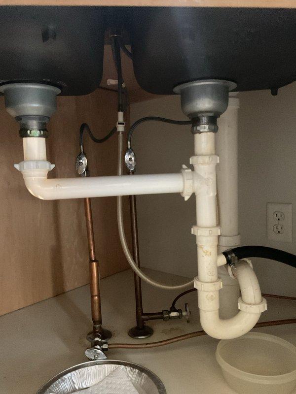 Responded to kitchen sink leak complaint affecting one side of double-bowl sink. Upon inspection, identified compromised drain piping beneath sink causing water leakage and rendering one basin unusable. Removed existing white PVC drainage system including dual P-traps, horizontal drain connections, and all associated fittings. Installed complete new drain pipe assembly with proper trap configuration for both disposal units, ensuring correct fall and venting. Verified all compression fittings and slip joints were properly sealed. Tested both sink basins and garbage disposals under full water flow to confirm leak-free operation and proper drainage. Both sides of sink restored to full functionality with all new piping installed per plumbing code requirements.