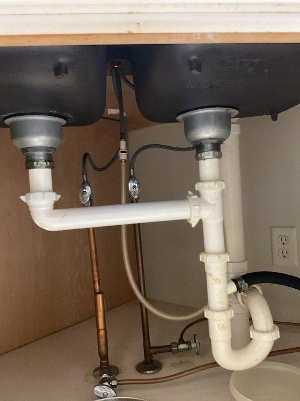 Responded to kitchen sink leak complaint affecting one side of double-bowl sink. Upon inspection, identified compromised drain piping beneath sink causing water leakage and rendering one basin unusable. Removed existing white PVC drainage system including dual P-traps, horizontal drain connections, and all associated fittings. Installed complete new drain pipe assembly with proper trap configuration for both disposal units, ensuring correct fall and venting. Verified all compression fittings and slip joints were properly sealed. Tested both sink basins and garbage disposals under full water flow to confirm leak-free operation and proper drainage. Both sides of sink restored to full functionality with all new piping installed per plumbing code requirements.