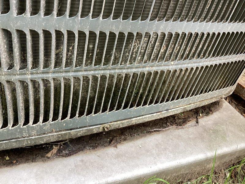 Completed annual cooling maintenance on 14-year-old Goodman air conditioning system with condenser motor replaced in 2022. Performed comprehensive tune-up inspection including visual assessment of outdoor condenser unit, which revealed significant accumulation of dirt, dust, and organic debris throughout the heat exchanger fins and coil surfaces. Documented heavy environmental soiling with brown discoloration and grime buildup, particularly in center and lower sections of the condenser coil, along with leaves and plant matter collected at the base where unit meets concrete pad. System operational and ready for cooling season.