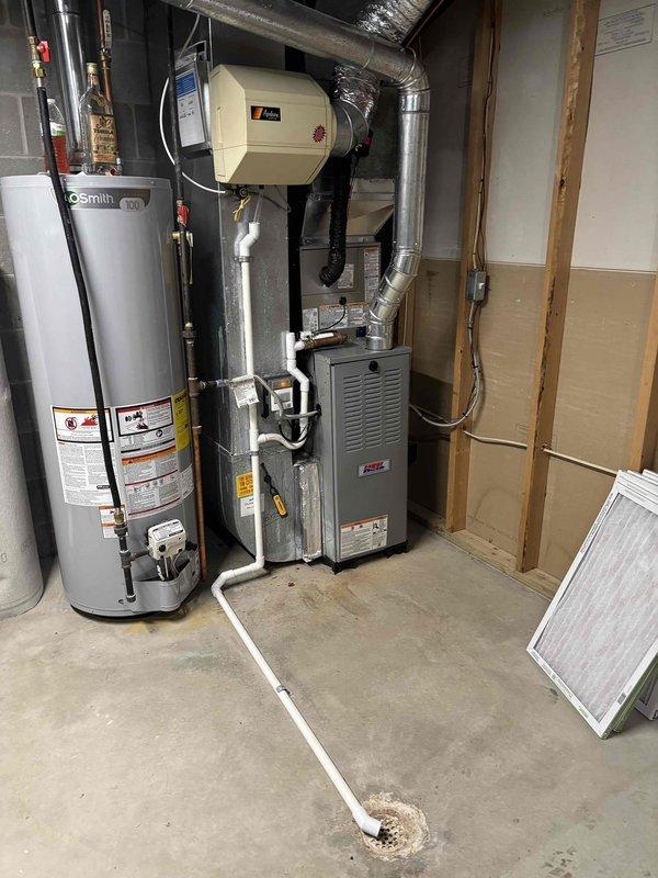 Completed full air conditioning system replacement at residential property. Removed existing outdoor condenser unit and installed new Carrier brand AC condenser on concrete pad against exterior wall with proper electrical connections via conduit mounted to siding. Unit positioned on decorative stone base for drainage and accessibility. Indoor components integrated with existing furnace and ductwork system in basement mechanical room, connecting to established humidifier and water heater infrastructure. All refrigerant lines, electrical connections, and condensate drainage properly installed and tested for optimal system performance.