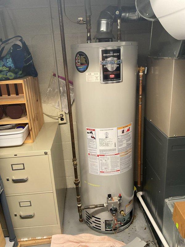 Responded to water heater leak in basement of 1965-built home. Upon inspection, found Bradford White water heater with active leak at base of unit. Documented existing installation with photos showing water heater connections, copper and black piping, pressure relief valve, and gas control assembly. Assessed leak source and provided customer with repair options and recommendations for addressing the water intrusion issue.