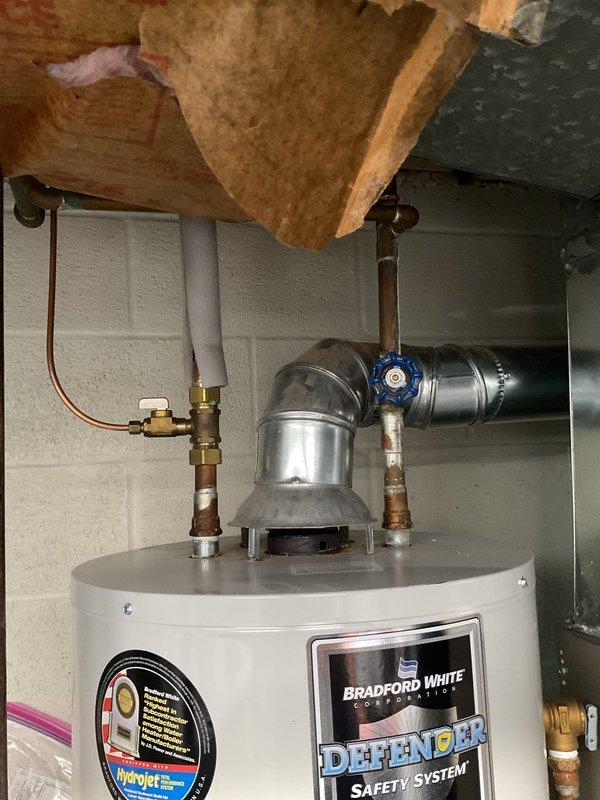 Responded to water heater leak in basement of 1965-built home. Upon inspection, found Bradford White water heater with active leak at base of unit. Documented existing installation with photos showing water heater connections, copper and black piping, pressure relief valve, and gas control assembly. Assessed leak source and provided customer with repair options and recommendations for addressing the water intrusion issue.