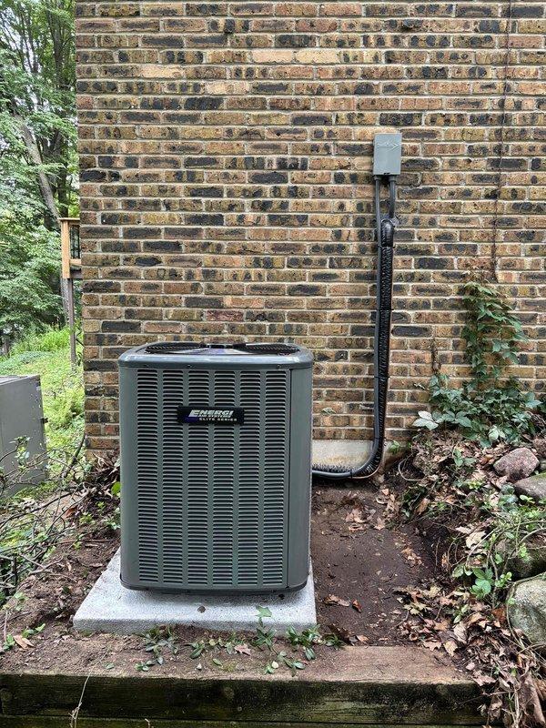 Completed full installation of new furnace and air conditioning system at residential property. Outdoor condenser unit installed on concrete pad against exterior brick wall with proper refrigerant line set routing and electrical disconnect box mounted per code requirements. All equipment secured, connected, and positioned for optimal performance with appropriate clearances maintained for service access and airflow.