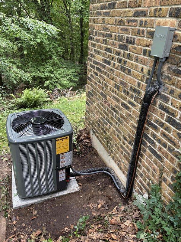 Completed full installation of new furnace and air conditioning system at residential property. Outdoor condenser unit installed on concrete pad against exterior brick wall with proper refrigerant line set routing and electrical disconnect box mounted per code requirements. All equipment secured, connected, and positioned for optimal performance with appropriate clearances maintained for service access and airflow.