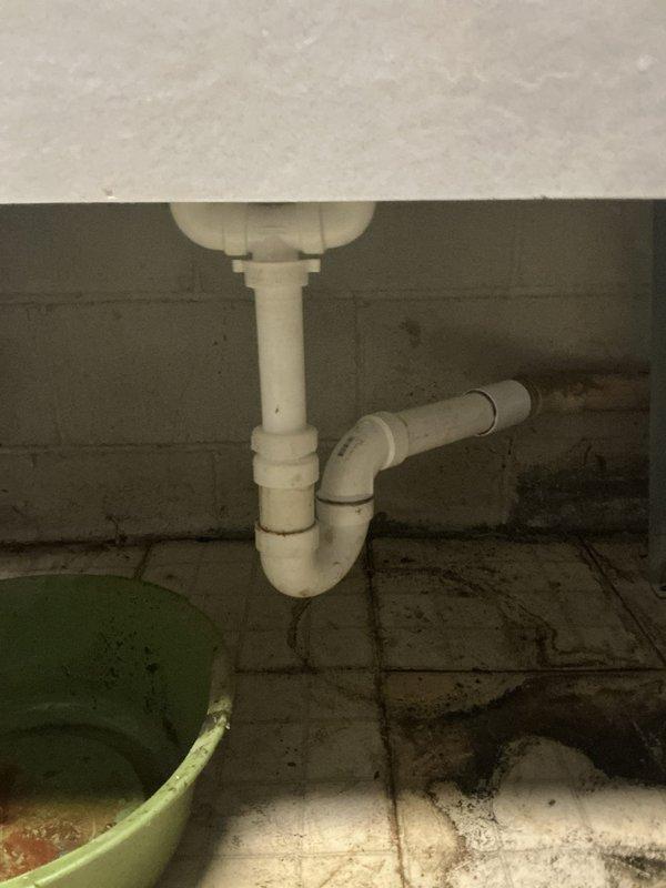 Completed installation of new white double-basin laundry sink with updated plumbing configuration including copper supply lines, brass boiler drain valves with yellow handles, PEX connections, flexible supply hoses, and new PVC P-trap drainage system mounted against concrete block wall in utility area.