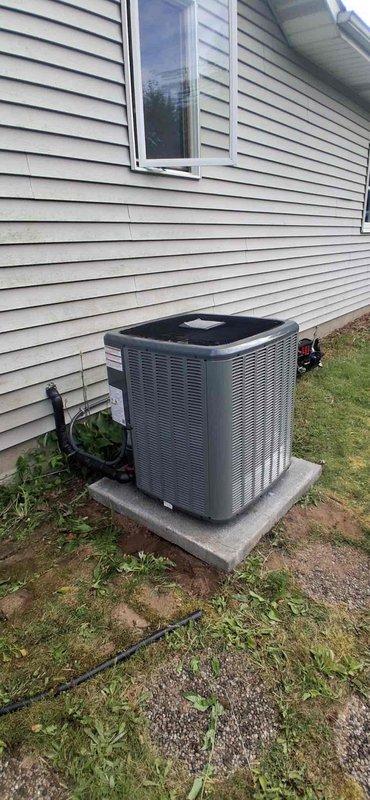 Completed full air conditioning system replacement at residential property. Removed existing condenser unit and installed new gray/silver AC condensing unit on existing concrete pad adjacent to house exterior with light tan vinyl siding. Connected refrigerant lines and electrical conduit from new condenser to indoor air handler. Verified proper placement on level concrete base, tested all electrical connections, and confirmed system operation. Unit installation includes protective mesh grille housing and manufacturer specifications compliance. All refrigerant lines properly insulated and secured to building structure.