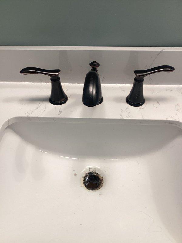 Completed replacement of widespread bathroom faucet assembly on undermount sink with marble-patterned countertop. Removed existing three-piece faucet set and installed new matte black widespread faucet with dual lever handles and center spout, ensuring proper mounting, supply line connections, and drain assembly functionality.