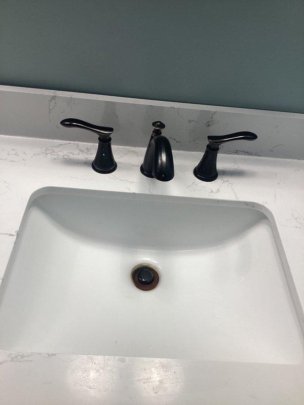 Completed replacement of widespread bathroom faucet assembly on undermount sink with marble-patterned countertop. Removed existing three-piece faucet set and installed new matte black widespread faucet with dual lever handles and center spout, ensuring proper mounting, supply line connections, and drain assembly functionality.