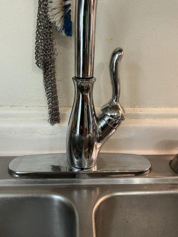Responded to service call for newly installed kitchen faucet that was loose and unstable at mounting point. Tightened mounting hardware and securing nut beneath sink deck to properly stabilize the single-handle chrome faucet assembly on the stainless steel sink basin, ensuring fixture was secure and operational.