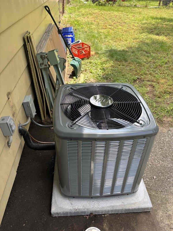 Completed full residential air conditioning system replacement at single-family home. Removed existing condensing unit and installed new gray/silver outdoor AC condenser on concrete pad adjacent to yellow vinyl-sided exterior. Properly mounted electrical disconnect box on exterior wall, ran refrigerant lines and electrical conduit through siding penetration, and secured all connections per manufacturer specifications. Verified unit placement on level concrete pad, tested system operation, and confirmed all warning labels and specifications were clearly visible on equipment. Installation completed as same-day service with all components functioning properly upon final inspection.