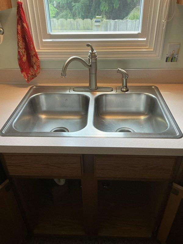 Completed kitchen sink replacement in 32-year-old residence. Installed new double-basin stainless steel sink with single-handle faucet in brushed nickel finish and separate spray nozzace assembly. Configured standard PVC drain assembly with P-trap beneath sink, ensuring proper drainage and code-compliant installation. All plumbing connections tested and verified leak-free upon completion.