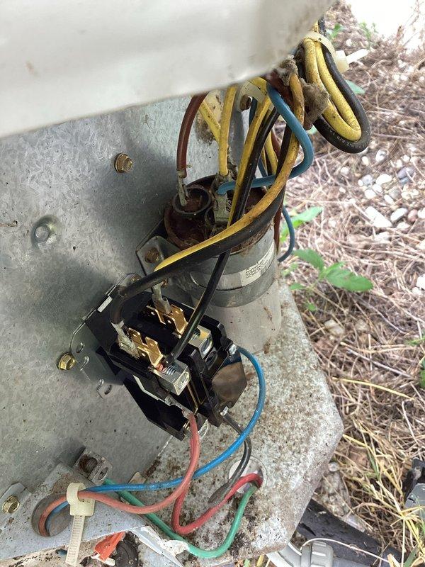 Responded to service call for air conditioning system malfunction. Upon arrival, performed visual inspection of outdoor condenser unit and electrical components. Found aging electrical assembly with weathered wiring, contactor, and capacitor showing signs of deterioration and exposure to elements. Wiring insulation displayed fading and wear consistent with extended outdoor exposure. Condenser unit exterior exhibited rust staining and corrosion on top surface and fan guard, indicating need for maintenance attention. Electrical connections appeared disorganized with coiled wire bundling. Documented equipment condition through photographs for service records. Unit located in overgrown landscaping area with vegetation encroachment around condenser, potentially restricting airflow. Assessed overall system condition and identified components requiring monitoring or replacement to ensure continued reliable operation.