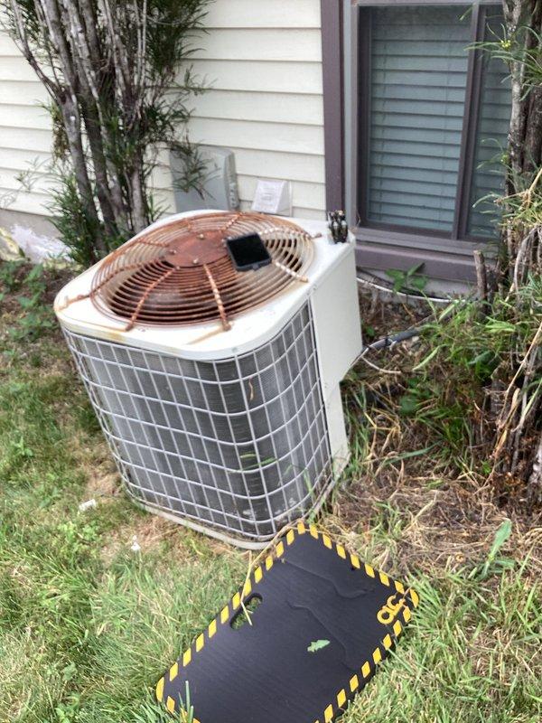 Responded to service call for air conditioning system malfunction. Upon arrival, performed visual inspection of outdoor condenser unit and electrical components. Found aging electrical assembly with weathered wiring, contactor, and capacitor showing signs of deterioration and exposure to elements. Wiring insulation displayed fading and wear consistent with extended outdoor exposure. Condenser unit exterior exhibited rust staining and corrosion on top surface and fan guard, indicating need for maintenance attention. Electrical connections appeared disorganized with coiled wire bundling. Documented equipment condition through photographs for service records. Unit located in overgrown landscaping area with vegetation encroachment around condenser, potentially restricting airflow. Assessed overall system condition and identified components requiring monitoring or replacement to ensure continued reliable operation.