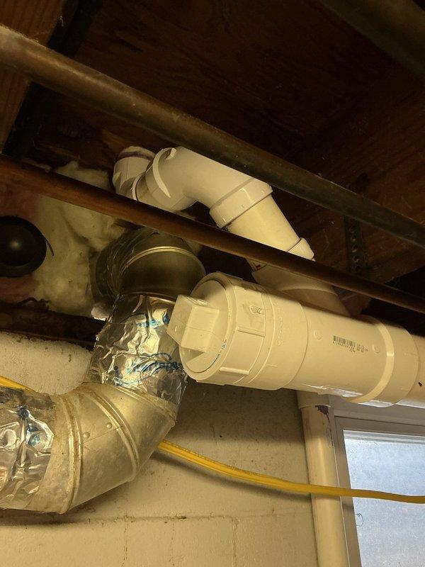 Completed repipe installation in basement area, replacing deteriorated metal piping with new white PVC drainage system. Installed proper fittings including 90-degree elbows and Y-junction connections, transitioning from new PVC to existing cast iron waste line using rubber coupling adapter. Work performed beneath floor joists with proper routing and support to ensure code-compliant installation and optimal drainage flow.