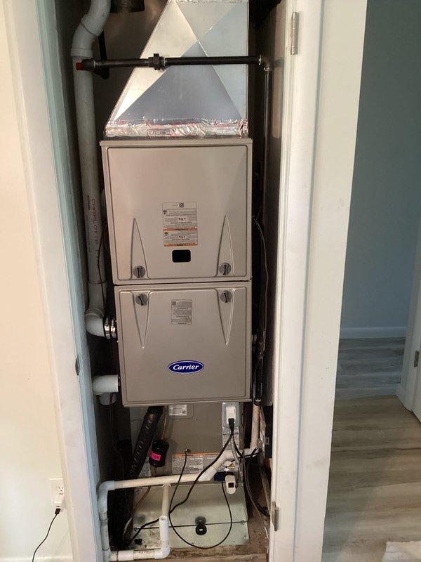 Completed full HVAC system installation including indoor Carrier furnace unit and outdoor condensing unit. Indoor furnace was installed in utility closet with proper ductwork connections, PVC condensate drain lines, refrigerant line set, and electrical wiring. Outdoor condenser was positioned on concrete pad against building exterior with electrical disconnect box mounted to wall and conduit properly secured. All components tested and verified operational upon completion.