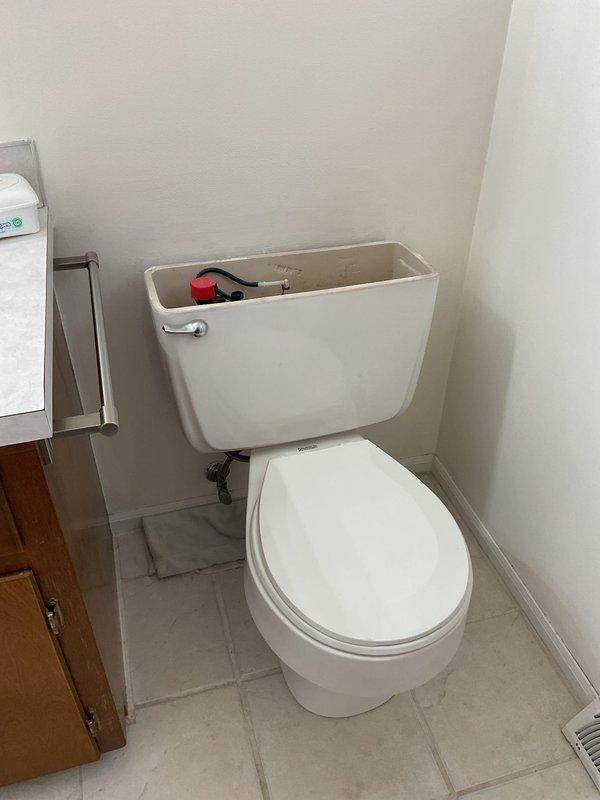 Responded to service call for toilet leaking at base of tank with water pooling on floor when flushed, ongoing issue for approximately two weeks in 48-year-old home. Upon arrival, inspected two-piece toilet and identified leak originating from tank-to-bowl connection. Examined tank components including flush valve mechanism and supply line connections. Assessed water damage to floor area and confirmed leak occurred during flush cycle. Documented existing conditions with photographs showing toilet installation, floor-mounted supply line with shut-off valve, and evidence of water exposure on tile flooring. Addressed primary concern of foreign object (dentures) flushed down toilet that may have contributed to initial plumbing disturbance.