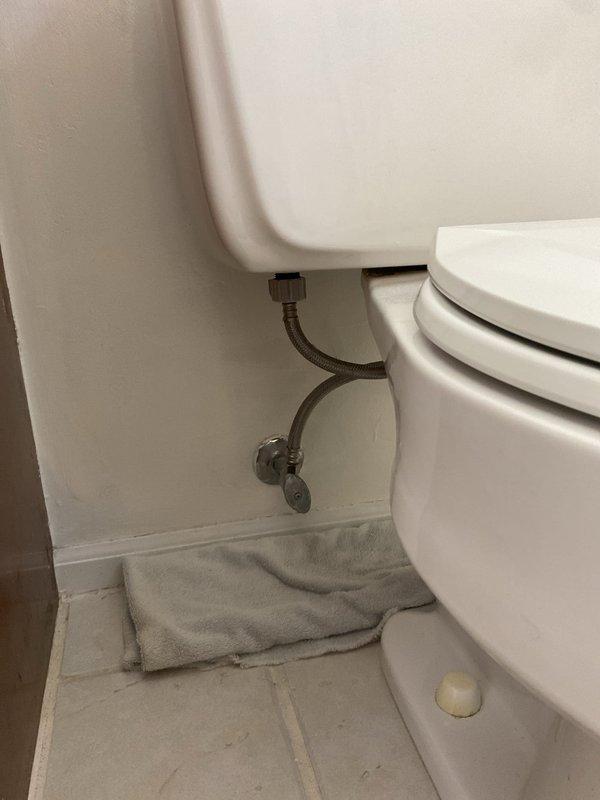 Responded to service call for toilet leaking at base of tank with water pooling on floor when flushed, ongoing issue for approximately two weeks in 48-year-old home. Upon arrival, inspected two-piece toilet and identified leak originating from tank-to-bowl connection. Examined tank components including flush valve mechanism and supply line connections. Assessed water damage to floor area and confirmed leak occurred during flush cycle. Documented existing conditions with photographs showing toilet installation, floor-mounted supply line with shut-off valve, and evidence of water exposure on tile flooring. Addressed primary concern of foreign object (dentures) flushed down toilet that may have contributed to initial plumbing disturbance.