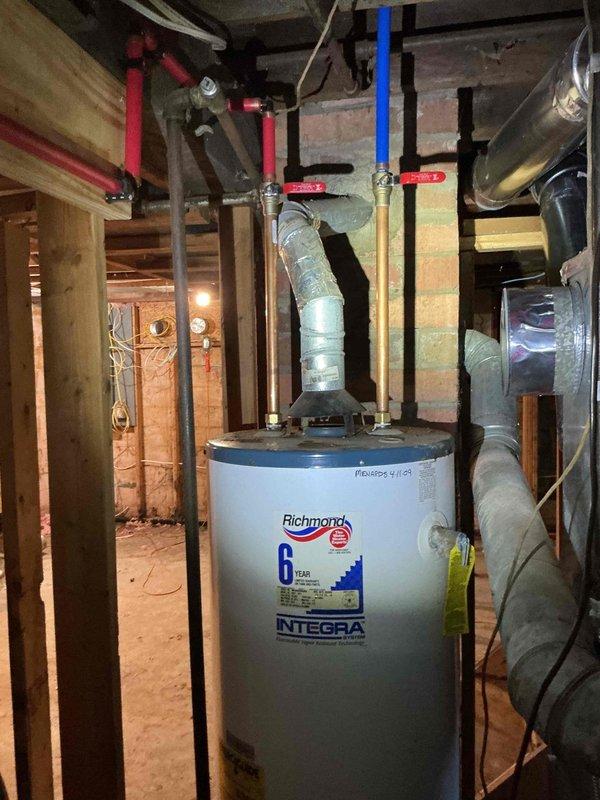 Responded to service call for tankless water heater installation. Upon arrival, found customer had purchased new tankless unit requiring professional installation. However, assessment revealed existing Richmond Integra conventional tank water heater already installed in unfinished basement utility area with all plumbing connections, venting, and shut-off valves properly configured and operational. Consulted with customer regarding discrepancy between service request for tankless installation and current conventional tank system in place. Inspected existing installation including copper supply lines with red-handled valves, PEX connections, and metallic venting system - all components found to be code-compliant and functioning correctly. No tankless water heater installation performed as conventional unit already serving property.