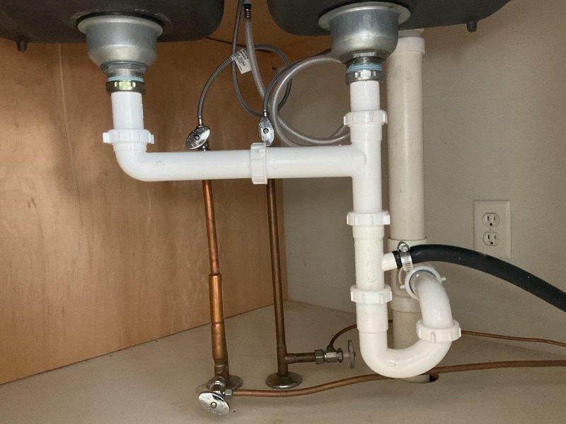 Completed rework of kitchen sink plumbing system including P-trap, tubular piping, and AAV installation under double-basin sink. Reconfigured drain assembly with proper horizontal connection between both basins, installed new white PVC P-trap with correct trap arm alignment to existing drain line. All connections secured with appropriate fittings and verified for proper drainage and leak-free operation. Customer-supplied faucet was previously installed and confirmed operational during service completion.