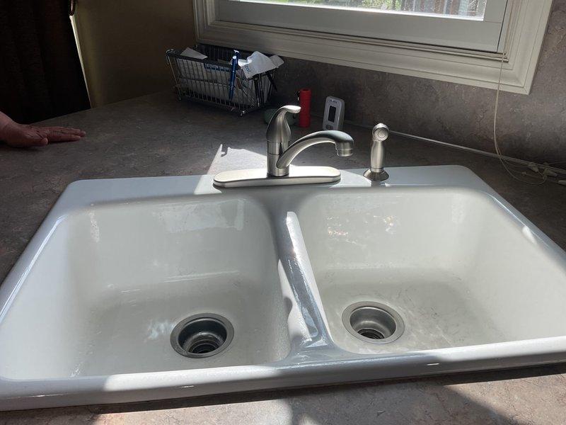 Completed rework of kitchen sink plumbing system including P-trap, tubular piping, and AAV installation under double-basin sink. Reconfigured drain assembly with proper horizontal connection between both basins, installed new white PVC P-trap with correct trap arm alignment to existing drain line. All connections secured with appropriate fittings and verified for proper drainage and leak-free operation. Customer-supplied faucet was previously installed and confirmed operational during service completion.