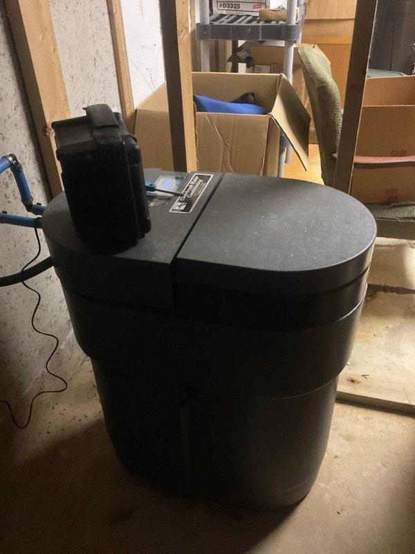 Responded to service call for non-functioning water softener system. Upon inspection, evaluated the brine tank and control unit setup in the basement utility area. Assessed the system components including the resin tank, control valve assembly, and brine tank configuration to diagnose operational issues. Documented existing installation conditions with photographic evidence showing the water softener equipment and surrounding mechanical space for service records.