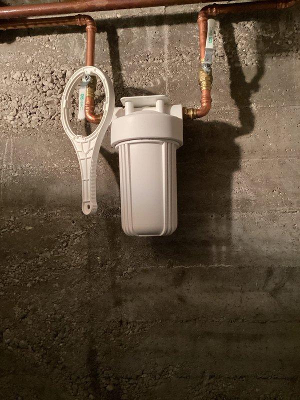 Removed existing water treatment equipment from basement utility area and completed installation of new Sterling high-efficiency water softener system with integrated whole house sediment filter. Configured copper supply piping with brass compression fittings and mounted white sediment filter housing to concrete wall with proper inlet/outlet connections. System installed, tested, and left operational with all components properly positioned and secured.
