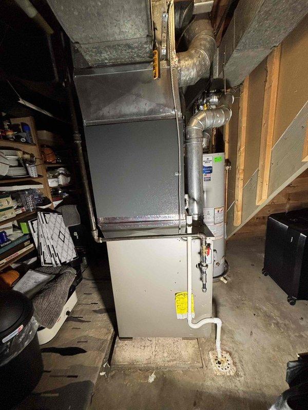 Completed full air conditioning system replacement in basement mechanical room. Removed existing AC unit and installed new HVAC system including furnace with integrated air handler and metal plenum assembly. Connected silver metal ductwork to ceiling distribution system with proper sealing at all joints. Verified all manufacturer specifications, safety labels, and operational plates were properly displayed on equipment. Ensured proper clearances around furnace unit and adjacent water heater for code compliance and serviceability. Tested system startup, confirmed proper airflow through ductwork, and verified all electrical and gas connections were secure and functioning correctly.