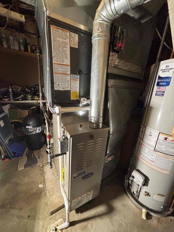 Completed full air conditioning system replacement in basement mechanical room. Removed existing AC unit and installed new HVAC system including furnace with integrated air handler and metal plenum assembly. Connected silver metal ductwork to ceiling distribution system with proper sealing at all joints. Verified all manufacturer specifications, safety labels, and operational plates were properly displayed on equipment. Ensured proper clearances around furnace unit and adjacent water heater for code compliance and serviceability. Tested system startup, confirmed proper airflow through ductwork, and verified all electrical and gas connections were secure and functioning correctly.