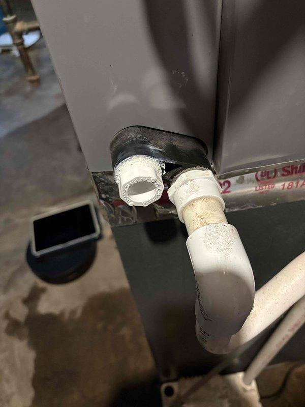 Responded to water leak complaint near furnace area. Upon inspection, identified water accumulation originating from condensate drain system. Found compromised PVC condensate line connection with black rubber coupling showing signs of deterioration and improper seal. Measured condensate pump operation at 120V confirming electrical function. Documented failed drain connection beneath equipment where dirt and grime buildup indicated ongoing moisture issue. Provided thermostat operation instruction to address client's control system concerns.
