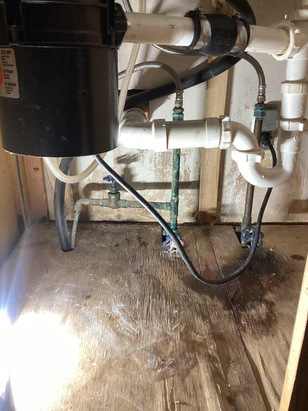 Responded to reported leak in wall. Removed section of drywall to access plumbing behind kitchen sink cabinet. Upon inspection, identified corrosion and oxidation on copper supply fittings and connections beneath sink, with visible water staining on cabinet floor indicating previous moisture intrusion. Documented existing plumbing conditions including garbage disposal installation, PVC drain assembly, braided supply lines, and corroded shut-off valves with green handles. Inspected outdoor spigot as requested and verified operational status. Secured all accessible plumbing connections and advised on condition of aging fixtures showing significant wear and corrosion requiring future attention.