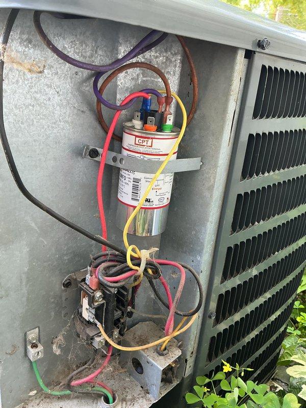 # CP-Cooling Problem Service Completion

Responded to service call for 15-year-old air conditioning system experiencing excessive noise and inability to maintain consistent temperature setpoint. Upon arrival, performed diagnostic evaluation of outdoor condensing unit. Removed access panel to inspect electrical components and internal systems. 

Visual inspection revealed aged electrical components including capacitor and contactor assembly. Examined all wire connections at capacitor terminals, noting multiple colored conductors (red, yellow, purple, brown, green) secured to top terminals. Inspected contactor relay unit positioned below capacitor, verifying connection integrity of associated wiring. Assessed condition of condenser coil fins, which showed normal weathering consistent with outdoor equipment age.

Evaluated overall system operation and component functionality. Documented existing conditions through photographic records showing capacitor, contactor, wiring configuration, an