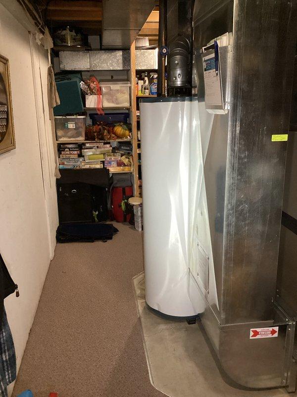 Completed water heater estimate for residential basement installation. Assessed existing white tank-style water heater with proper venting through metallic elbow duct connector, foam-insulated copper supply lines, and brass shut-off valving. Documented current installation configuration including proximity to HVAC furnace unit and available clearances within utility space for potential replacement considerations.