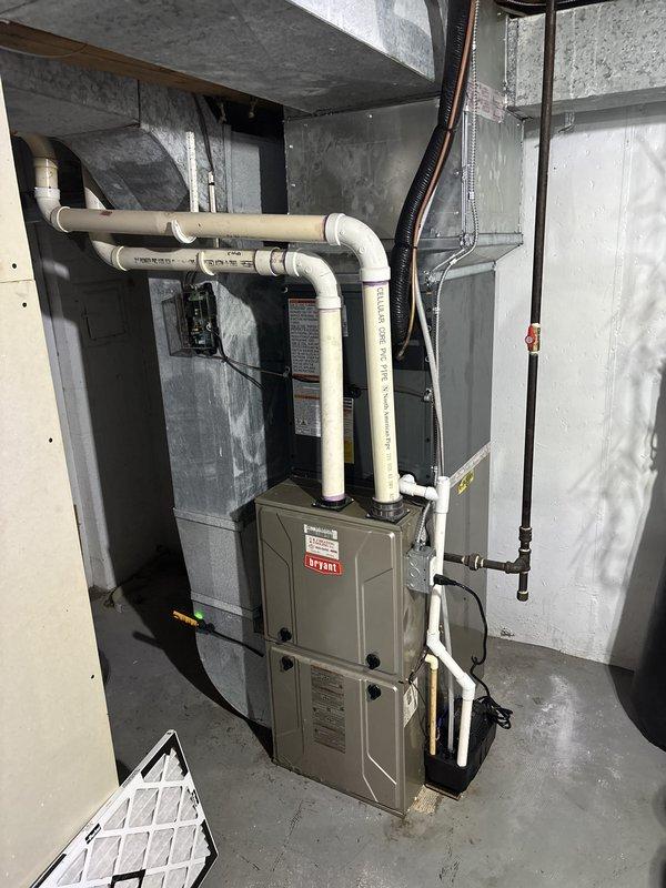 Completed full air conditioning system replacement including outdoor condenser unit and indoor air handler components. Installed new Bryant HVAC equipment in basement mechanical room with proper refrigerant line routing, condensate drainage system using white PVC piping with multiple elbows secured to ceiling joists, and electrical connections. Mounted outdoor condenser unit on concrete pad against exterior wall with refrigerant lines properly bracketed to building siding, verified all connections, and ensured system operational functionality upon completion.