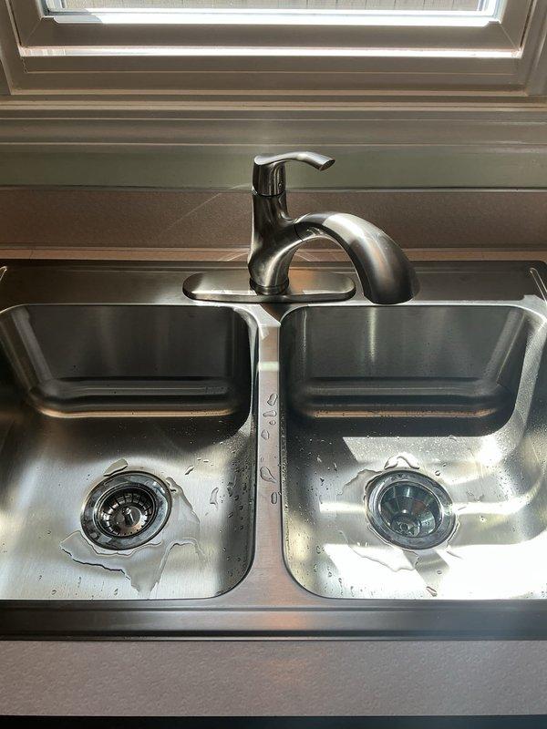 Completed installation of client-supplied double-basin stainless steel kitchen sink with bronze finish single-handle faucet. Connected all drain assemblies including P-trap configuration and verified proper water supply connections and drainage function.