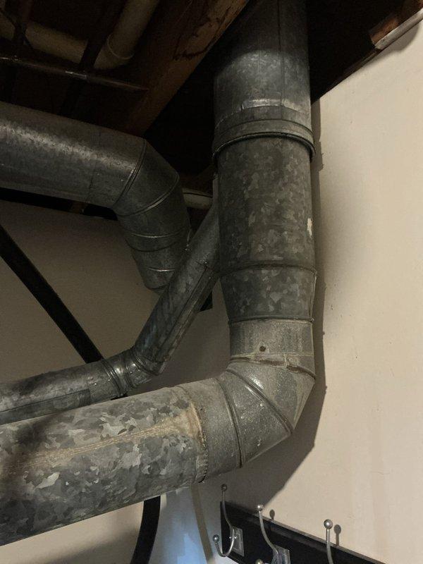 Completed comprehensive HVAC system assessment for air conditioning estimate at 6PM appointment. Documented existing galvanized metal ductwork configuration showing age-related wear and dust accumulation throughout ceiling-mounted ventilation pathways, along with installed air handler unit featuring diamond-pattern textured exterior panel and visible airflow directional indicators in utility space.
