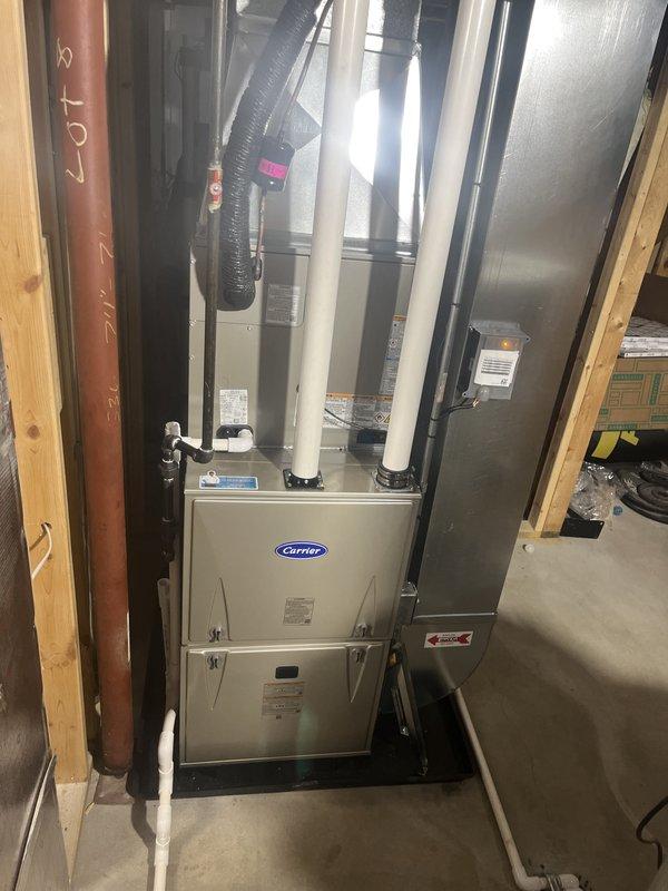 Completed full HVAC system installation including new Carrier brand furnace and air conditioning unit. Furnace installed in basement utility area with proper plenum connections, flexible and rigid ductwork integration, and PVC condensate drainage. Outdoor AC unit positioned on concrete pad against exterior wall with appropriate electrical connections, refrigerant line set, and conduit runs. All equipment mounted securely, tested for proper operation, and verified system functionality upon completion.