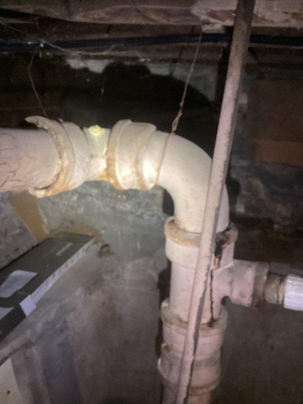 Conducted comprehensive plumbing evaluation of 1929-era residential property following home inspection findings. Assessed multiple plumbing valves requiring replacement throughout the home, examining both supply and drainage systems in basement and crawlspace areas. Documented existing conditions including aged PVC drainage piping with mineral deposits and discoloration at joints, gray pressure tank or filter housing components, and various copper supply lines with associated fittings. Evaluated insulated mechanical equipment, electrical connections, and utility infrastructure in confined access areas beneath the structure. Photographed all plumbing components, valve locations, and system configurations to provide detailed estimate for necessary repairs and replacements identified during the inspection process.