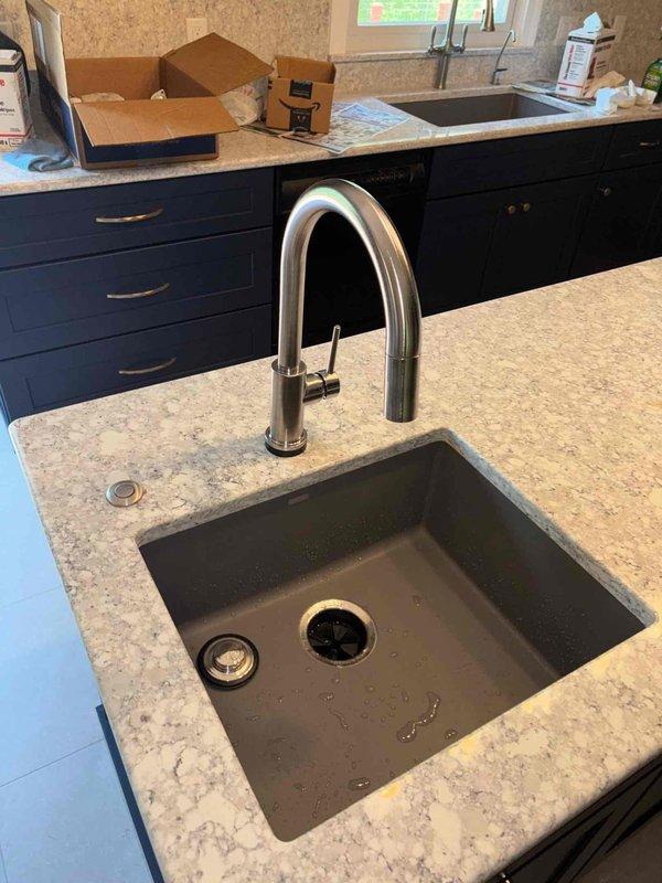Completed kitchen plumbing rough-in and finish work including installation of undermount sink with contemporary pull-down faucet, garbage disposal, and drain assembly in island countertop. Installed PVC drainage and vent piping through ceiling cavity with proper trap configurations, coordinated routing around existing electrical and structural framing members, then closed access openings to complete the project.