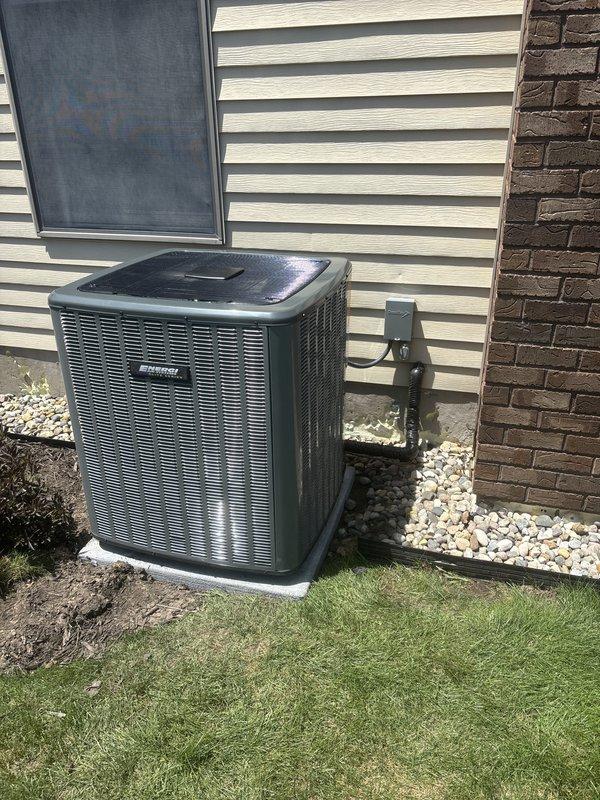 Completed full HVAC system installation including new furnace and air conditioning condenser unit. Installed outdoor AC condenser on concrete pad with proper electrical disconnect box and conduit connections, positioned unit against exterior wall with appropriate clearances and decorative stone landscaping for drainage. System installed per manufacturer specifications with all required refrigerant labeling, safety placards, and operational components properly secured and tested for functionality.